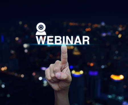 Hand pressing webinar button over blur night city tower background, Seminar online conceptの写真素材