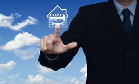 Businessman pressing hammer and wrench with house icon over blue sky with white clouds background,...