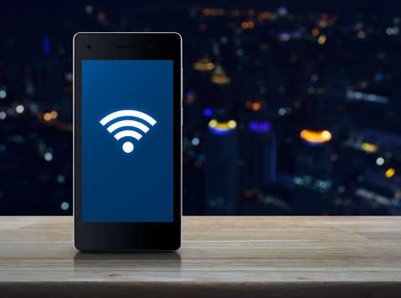 connection icon on modern smart phone screen on wooden table over blur light city tower, Technology and internet conceptの写真素材