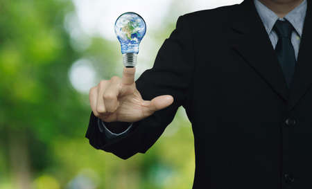 Businessman pressing earth globe in light bulb over blur green tree background, Energy conservation...