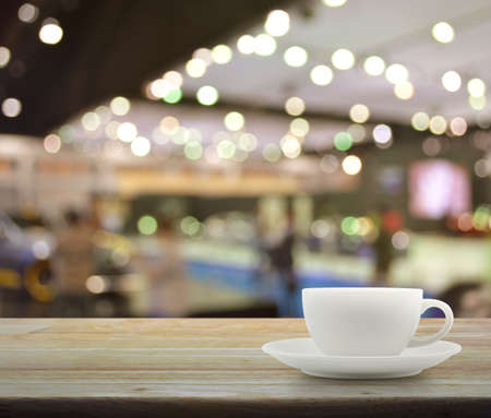 White cup on wooden table over blur of shopping mallの写真素材