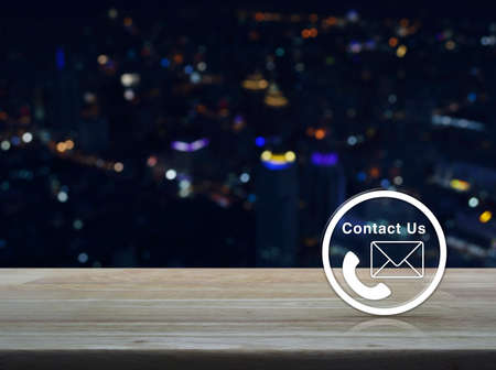 Telephone and mail icon button on wooden table over blur colourful night light city tower background, Contact us conceptの写真素材