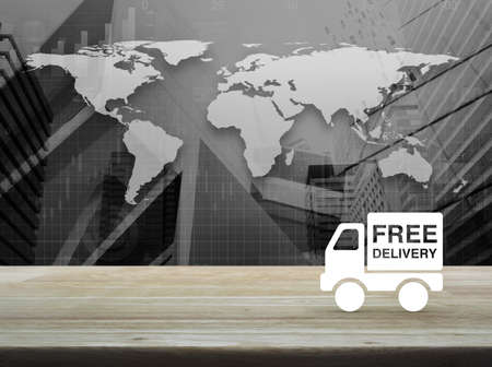 Free delivery truck icon on wooden table over black and white world map with financial graph and city tower, Transportation business conceptの写真素材