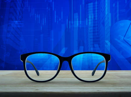Black eye glasses on wooden table over financial graph and city tower background, Business vision conceptの写真素材