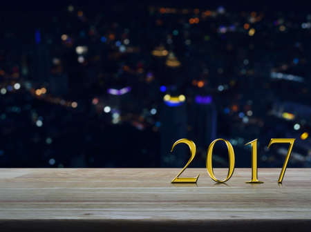 Happy new year 2017 gold metal text on wooden table over blur colourful night light city tower backgroundの写真素材