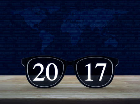 2017 text with eye glasses on wooden table over world map and computer binary code blue background,...
