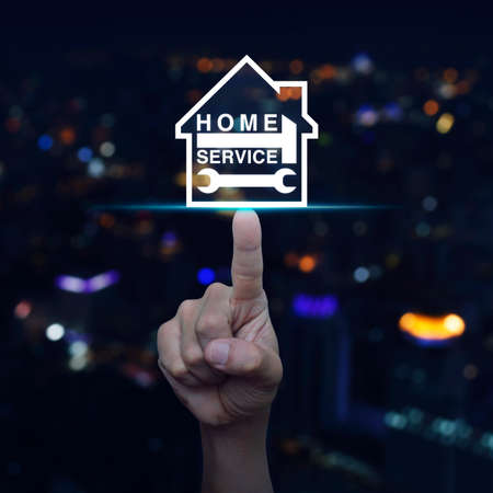Hand pressing hammer and wrench with house icon over blurred light city tower background, Home service conceptの写真素材