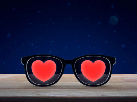 Love heart with eye glasses on wooden table over fantasy night sky and moon, Valentines day conceptの写真素材