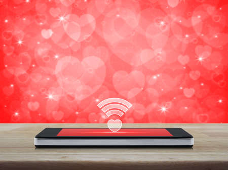 Heart wifi icon on modern smart phone screen on wooden table over blur red background, Internet online love connection, Valentines day conceptの写真素材