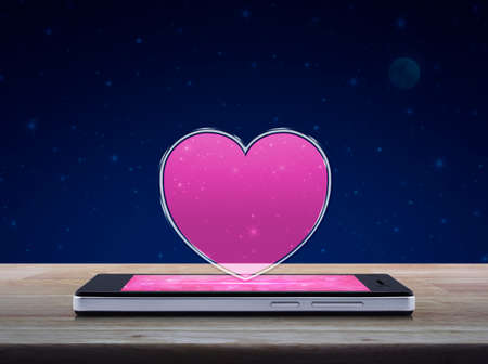 Love heart icon with copy space on modern smart phone screen on wooden table over fantasy night sky and moon, Internet online love connection, Valentines day conceptの写真素材