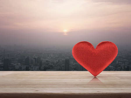 Fabric red love heart on wooden table over aerial view of cityscape at sunset, vintage style, Valentines day conceptの写真素材