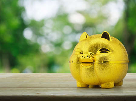 Gold piggy bank on wooden table over blur green tree background, Saving money conceptの写真素材