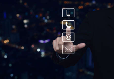 Businessman pressing telephone, mobile phone, at and email buttons over blur colorful night light city tower, Customer support conceptの写真素材