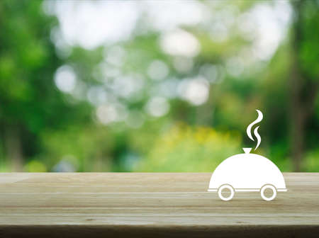Restaurant cloche flat icon on wooden table over blur green tree background, Food delivery conceptの写真素材