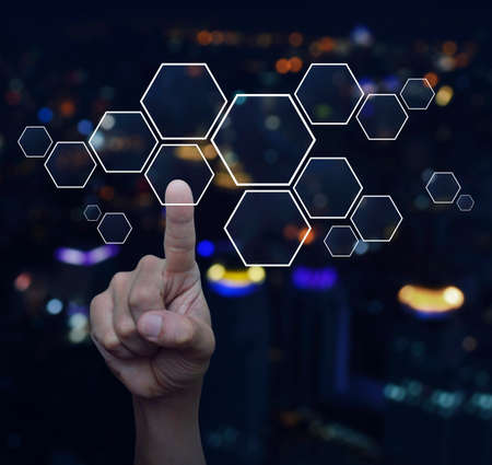 Hand pushing blank hexagon shape virtual technology screen over blur colorful night light city tower backgroundの写真素材