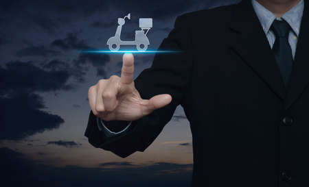 Businessman pressing motor bike icon over sunset sky, Business delivery service conceptの写真素材