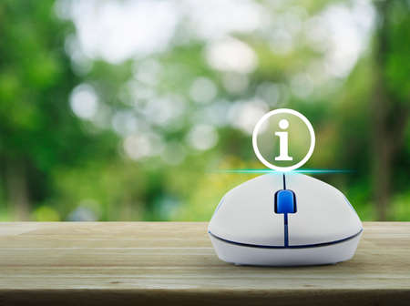 Information sign icon with wireless computer mouse on wooden table over blur green tree in park,...