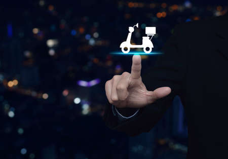 Businessman pressing motor bike icon over blur colorful night light city tower, Business delivery service conceptの写真素材