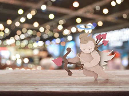 Cupid recycle paper craft on wooden table over blur light and shadow of shopping mall, Valentines...