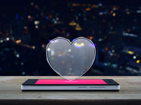 Love heart icon with copy space on modern smart phone screen on wooden table over blur colourful night light city tower, Internet online love connection, Valentines day conceptの写真素材