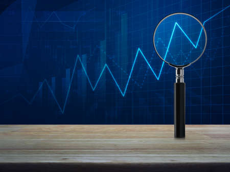 Magnifying glass with growth graph on wooden table over blue financial chart, Business success conceptの写真素材