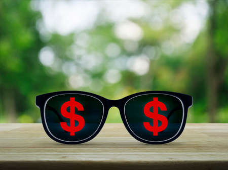 Dollar currency icon with eye glasses on wooden table over blur green tree background, Business...