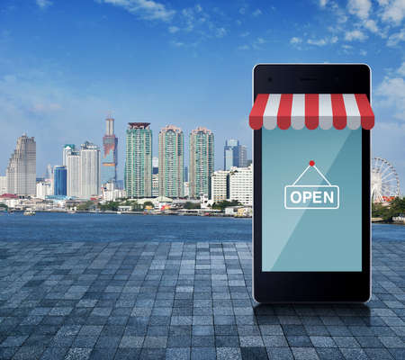 Modern smart mobile phone with on line shopping store graphic and open sign on stone tile floor over...