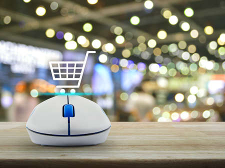 Shopping basket icon with wireless computer mouse on wooden table over blur light and shadow of shopping mall, Shop online conceptの写真素材