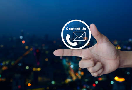 Telephone and mail icon button on finger over blur colorful night light city tower, Contact us conceptの写真素材