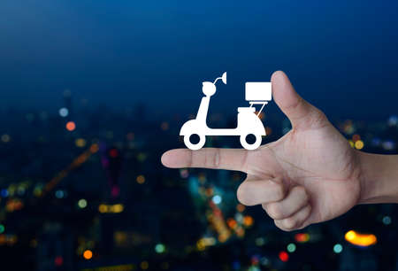Motor bike icon on finger over blur colorful night light city tower, Business delivery service conceptの写真素材