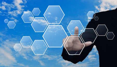 Businessman hand pushing blank hexagon shape virtual technology screen over blue sky with white cloudsの写真素材