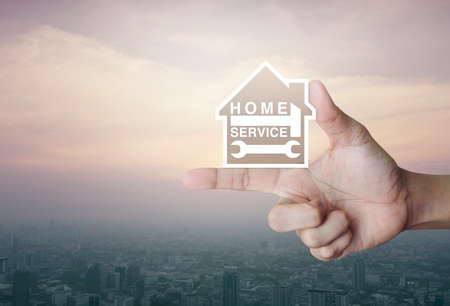 Hammer and wrench with house icon on finger over city tower at sunset, vintage style, Home service conceptの写真素材