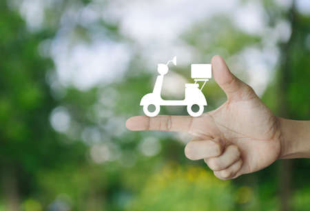 Motor bike icon on finger over blur green tree background, Business delivery service conceptの写真素材