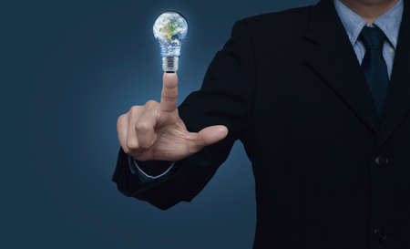 Businessman pressing earth globe in light bulb over blue background, Energy conservation and environmental conceptの写真素材