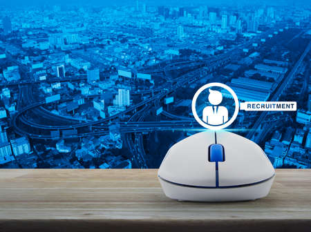 Businessman and magnifying glass icon with wireless computer mouse on wooden table over city tower,...