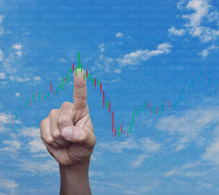 Hand pressing to trading graph of stock market over blue sky with white clouds, Business investment conceptの写真素材