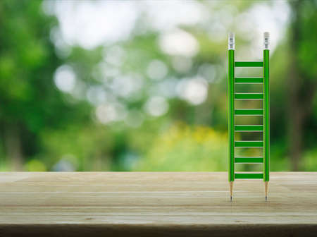 Green pencil ladder on wooden table over blur green tree in park, Business success conceptの写真素材