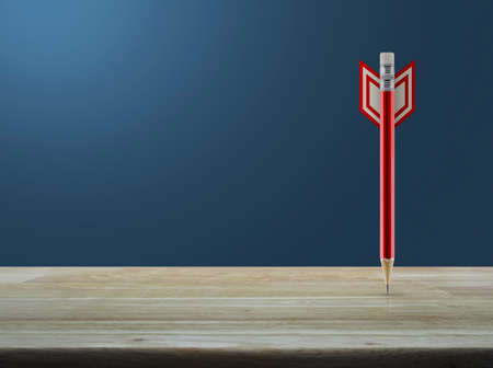 Red pencil in the shape of a dart on wooden table over light gradient blue background, Business...