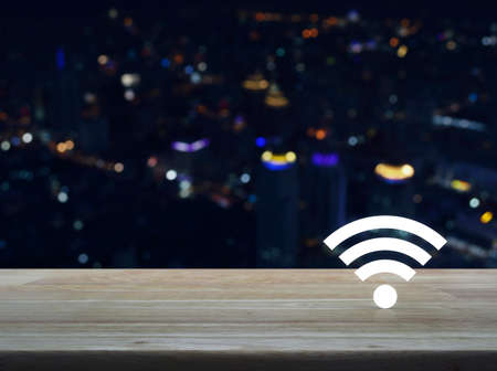 Wi-fi button on wooden table over blur colorful night light of modern city tower, Technology and internet conceptの写真素材