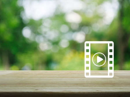 Play button with movie icon on wooden table over blur green tree, Cinema online conceptの写真素材