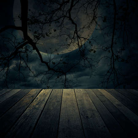 Old wooden table over dead tree, moon and spooky cloudy sky, Halloween backgroundの写真素材