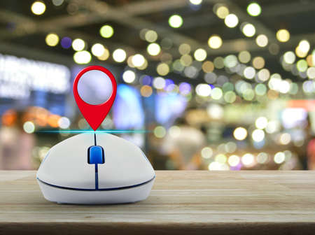 Map pin location button with wireless computer mouse on wooden table over blur light and shadow of shopping mall, Shopping navigation conceptの写真素材
