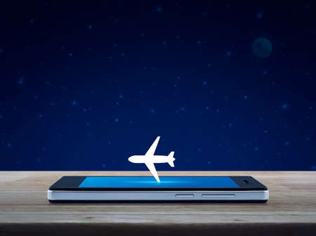 Airplane icon on modern smart phone screen on wooden table over fantasy night sky and moon, Business transportation conceptの写真素材