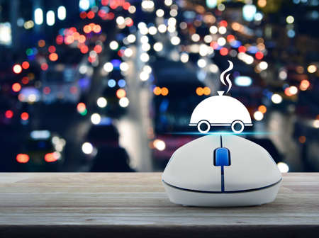 Restaurant cloche flat icon with wireless computer mouse on wooden table over blurred colourful night light city with cars, Food delivery conceptの写真素材