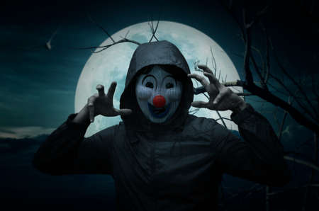 Scary evil clown wear jacket over bird, dead tree, moon and spooky cloudy sky, Halloween conceptの写真素材