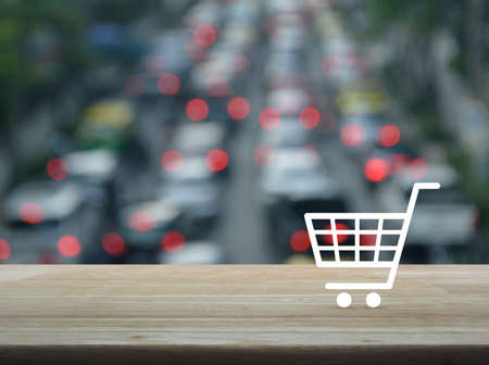 Shopping cart icon on wooden table over blur of rush hour with cars and road, Shop online conceptの写真素材