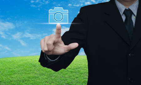 Businessman pressing camera flat icon over green grass field with blue sky, Business camera service conceptの写真素材
