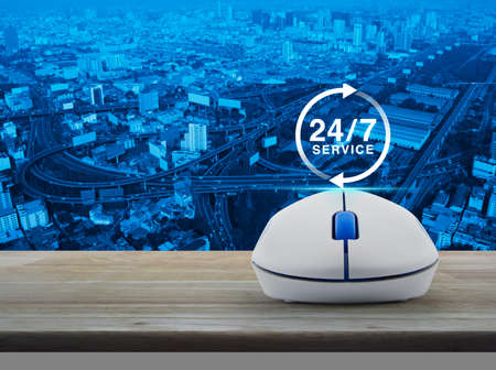 24 hours service icon with wireless computer mouse on wooden table over city tower, street and...