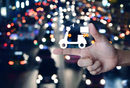 Motor bike icon on finger over blurred colourful night light city with cars, Business delivery service conceptの写真素材