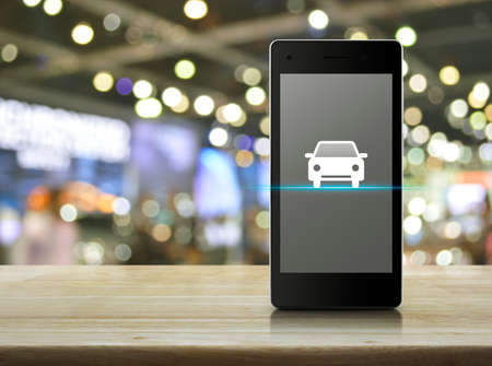 Taxi car flat icon on modern smart phone screen on wooden table over blur light and shadow of mall, Internet business service transportation conceptの写真素材